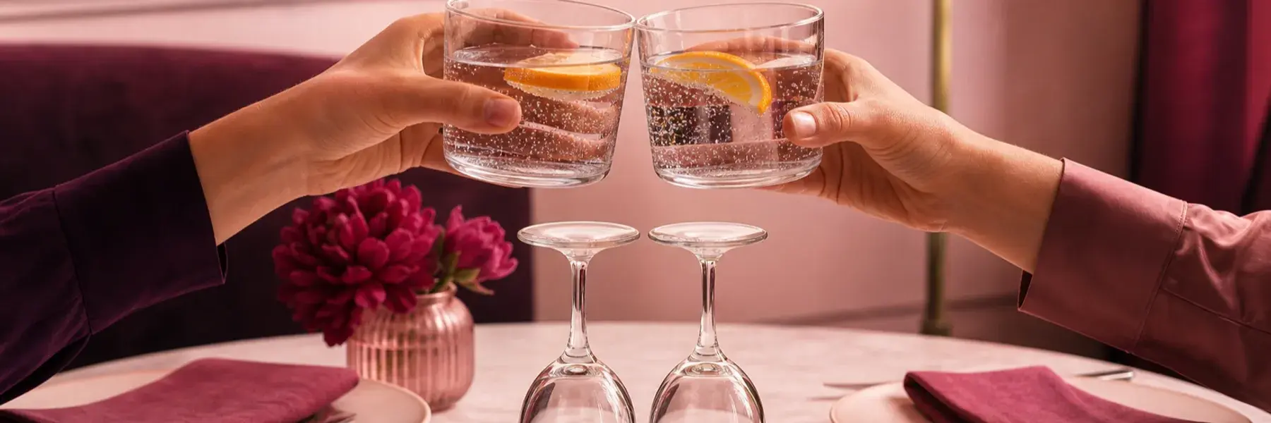 Two people toast sparkling citrus water beside unused inverted wine glasses on a date table.